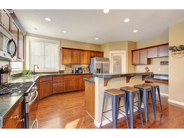a kitchen with stainless steel appliances granite countertop wooden cabinets a sink a stove a dining table and chairs