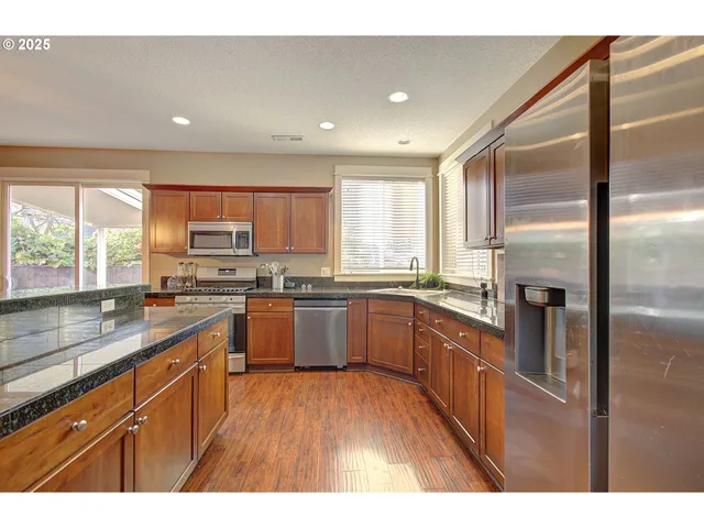 a kitchen with stainless steel appliances granite countertop a refrigerator a sink dishwasher a stove with wooden cabinets and floor