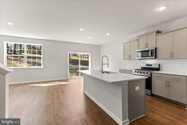 a kitchen with stainless steel appliances granite countertop a stove top oven a sink dishwasher and a refrigerator with wooden floor