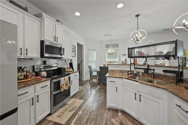 a kitchen with stainless steel appliances granite countertop a sink dishwasher stove and white cabinets with wooden floor