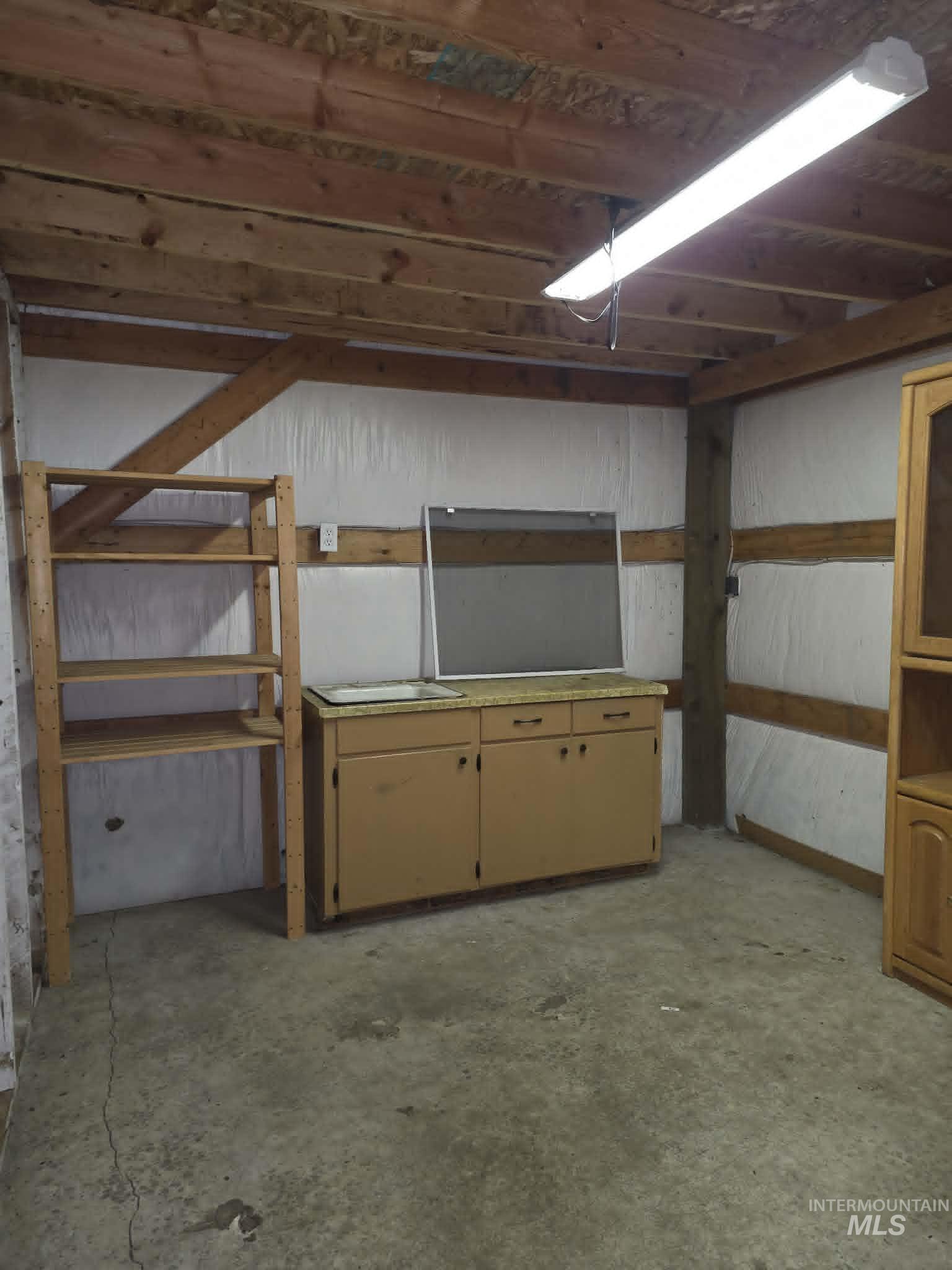Utility space featuring exposed wood beams, concrete flooring, and built-in cabinetry with a laminate countertop