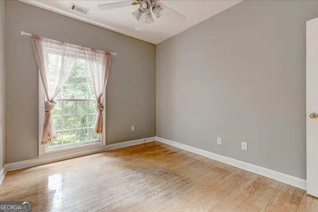 an empty room with wooden floor chandelier fan and windows