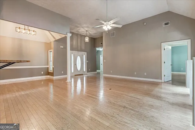 a view of an empty room with wooden floor and a kitchen