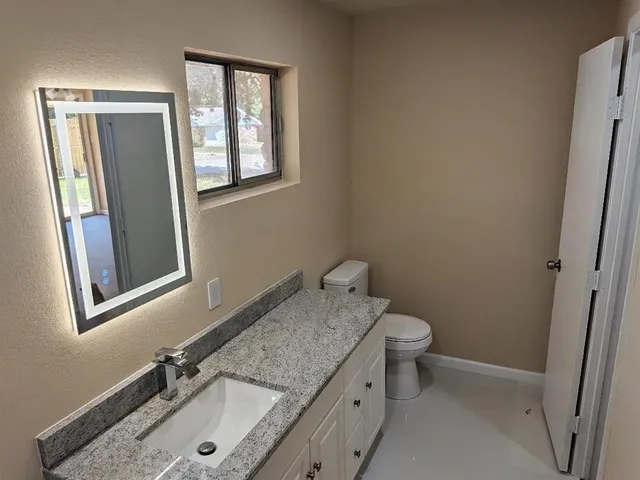a bathroom with a granite countertop sink toilet and mirror
