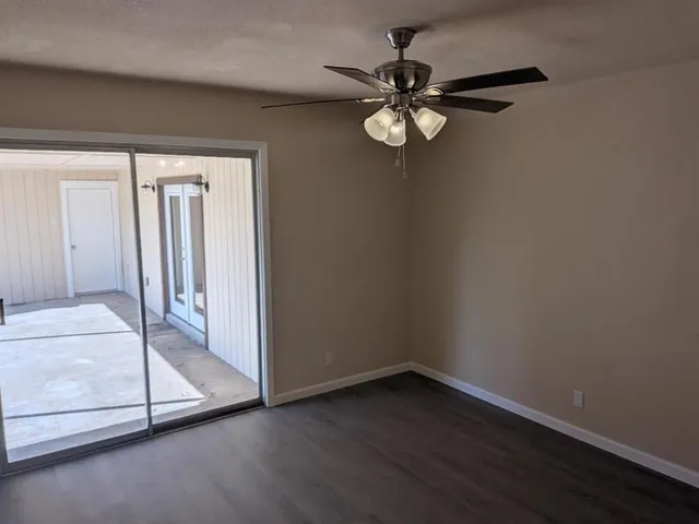 an empty room with wooden floor fan and windows
