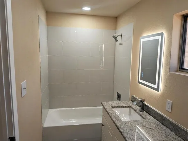 a bathroom with a granite countertop sink a mirror a bathtub and shower