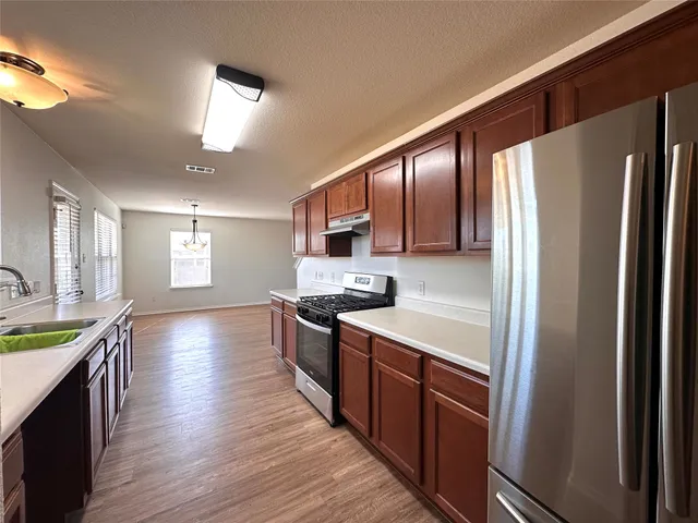 a large kitchen with stainless steel appliances granite countertop a refrigerator a sink dishwasher a stove and white countertops with wooden floor