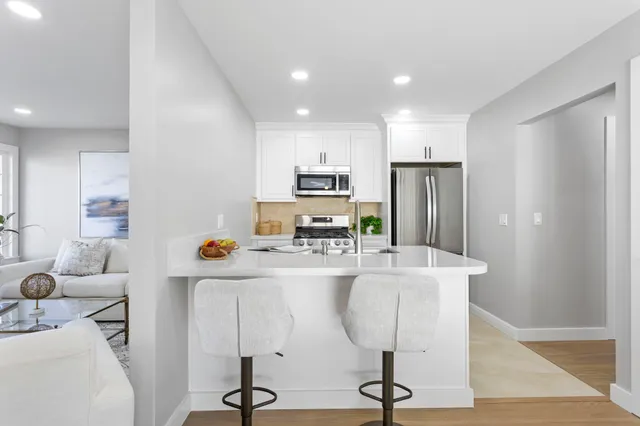 a kitchen with stainless steel appliances kitchen island granite countertop a refrigerator a stove a sink and white cabinets with wooden floor