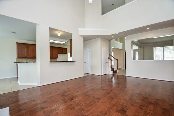 a view of an empty room with wooden floor and a kitchen