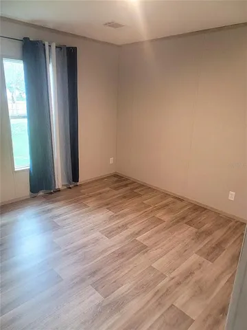 an empty room with wooden floor and windows with curtains