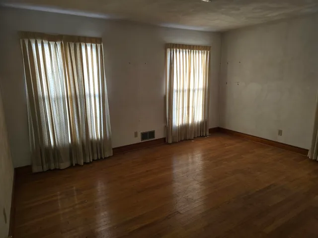 an empty room with wooden floor and windows with curtains