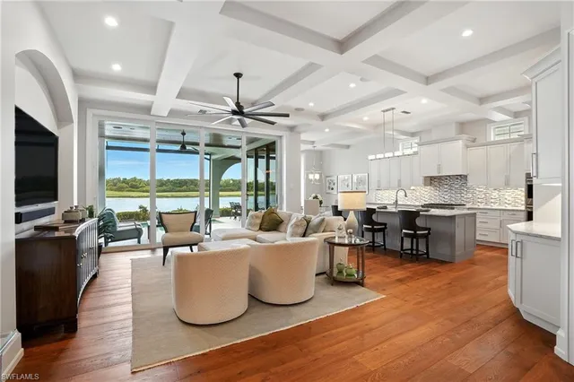 a living room with lots of furniture kitchen view and a large window