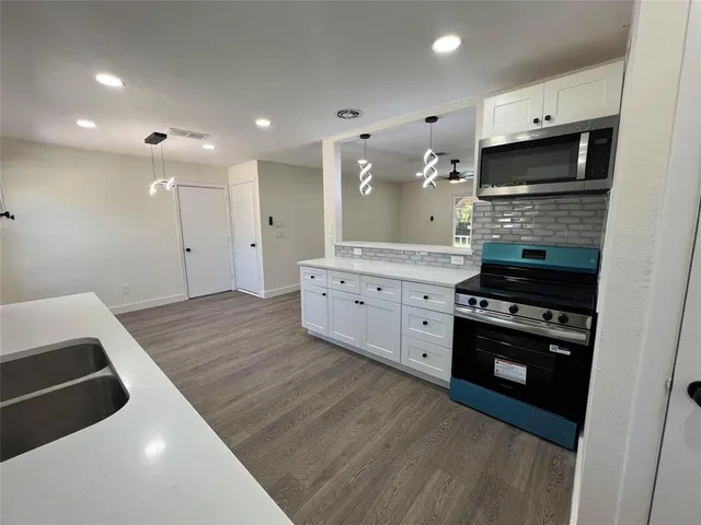 a kitchen with white cabinets a sink dishwasher and a stove with wooden floor