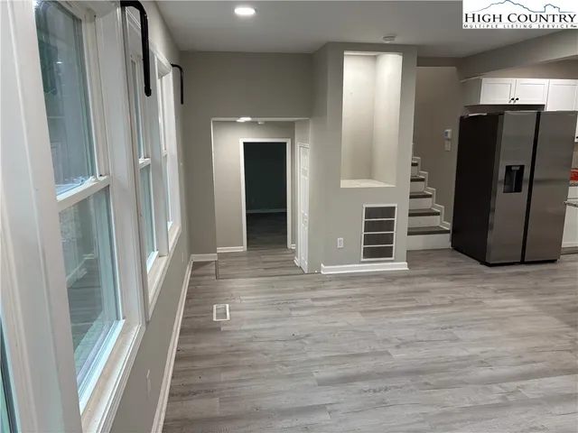a view of a refrigerator in kitchen and an empty room with wooden floor