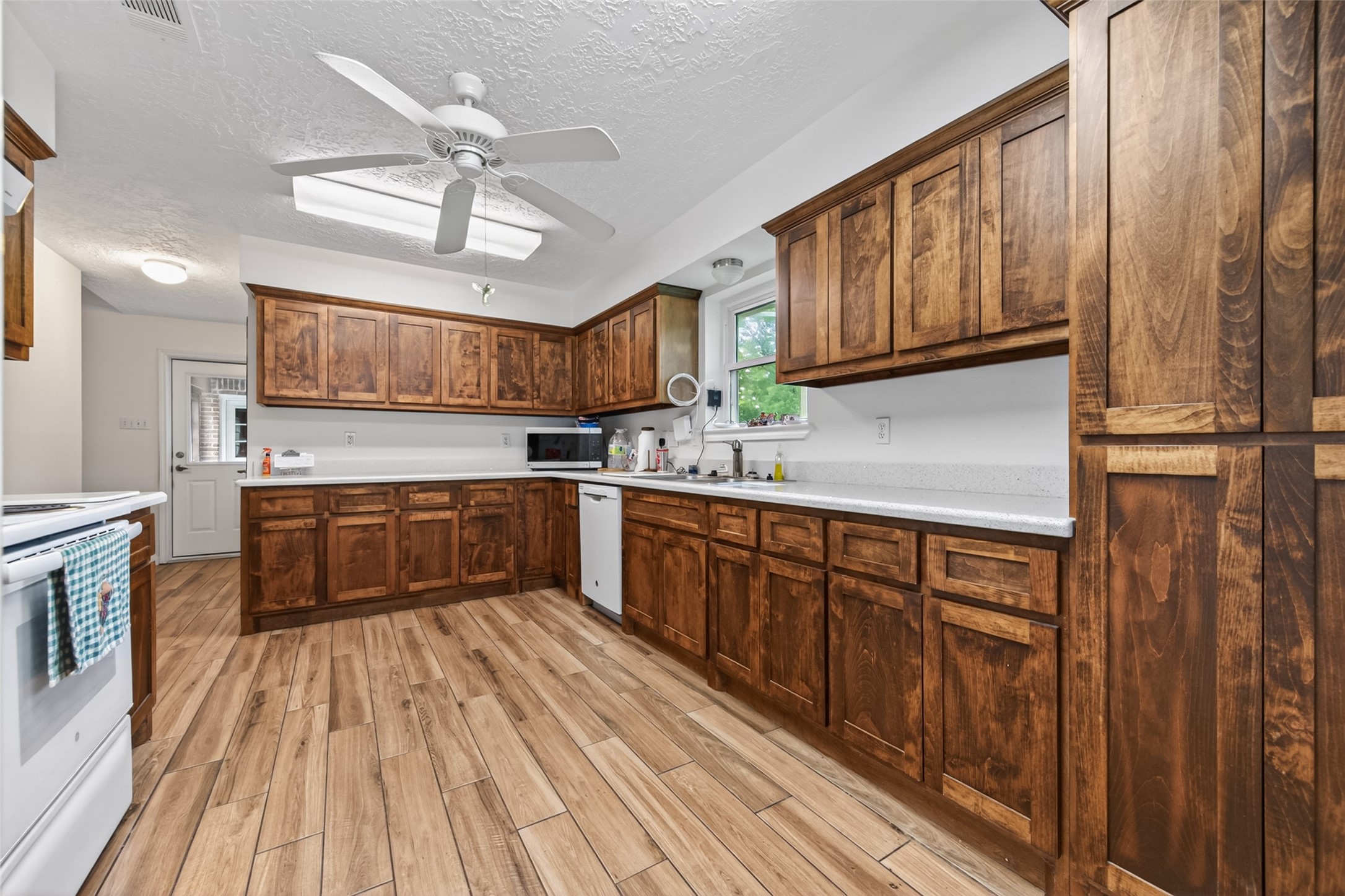 1004 Wagon Road Simonton, TX 77485 - Photo 13 of 40 This view showcases the kitchen's impressive U-shaped layout, with rich wood cabinetry wrapping the perimeter to maximize both storage and counter workspace. A window above the sink brings in natural light, while the ceiling fan with skylight keeps the space comfortable and bright. The layout flows easily toward the back door, adding everyday convenience.