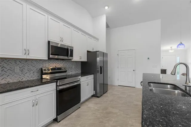 a kitchen with stainless steel appliances granite countertop a sink a stove top oven a refrigerator with white cabinets and granite countertops