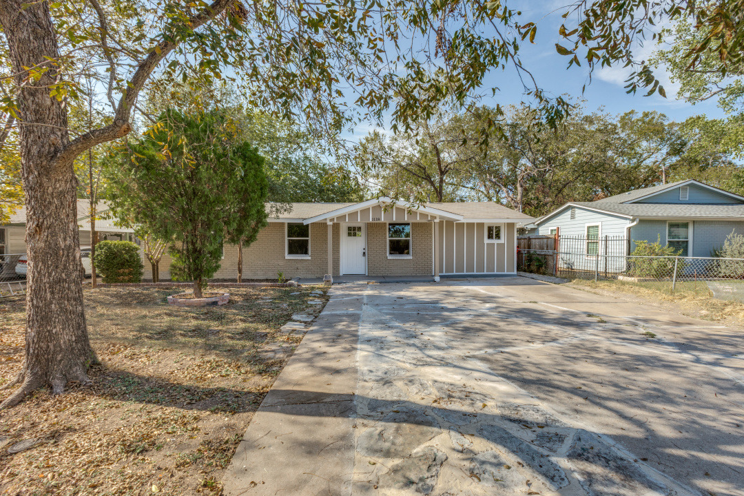 A classic ranch-style home features a spacious concrete driveway and mature trees gracing the yard.