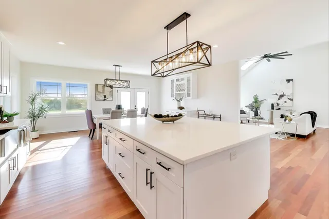 a kitchen with stainless steel appliances a white stove top oven a sink a dining table and chairs with wooden floor