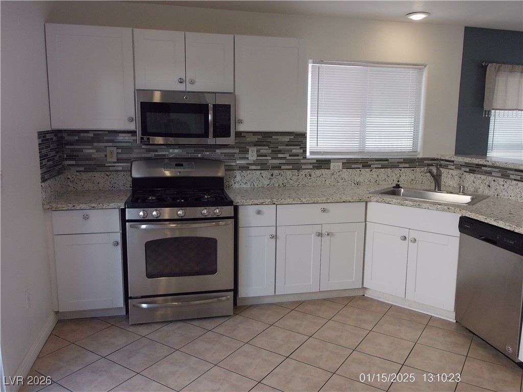 7332 Ribbon Ridge Avenue Las Vegas, NV 89129 - Photo 3 of 28 Kitchen featuring white cabinets, appliances with stainless steel finishes, light stone counters, light tile patterned floors, and tasteful backsplash