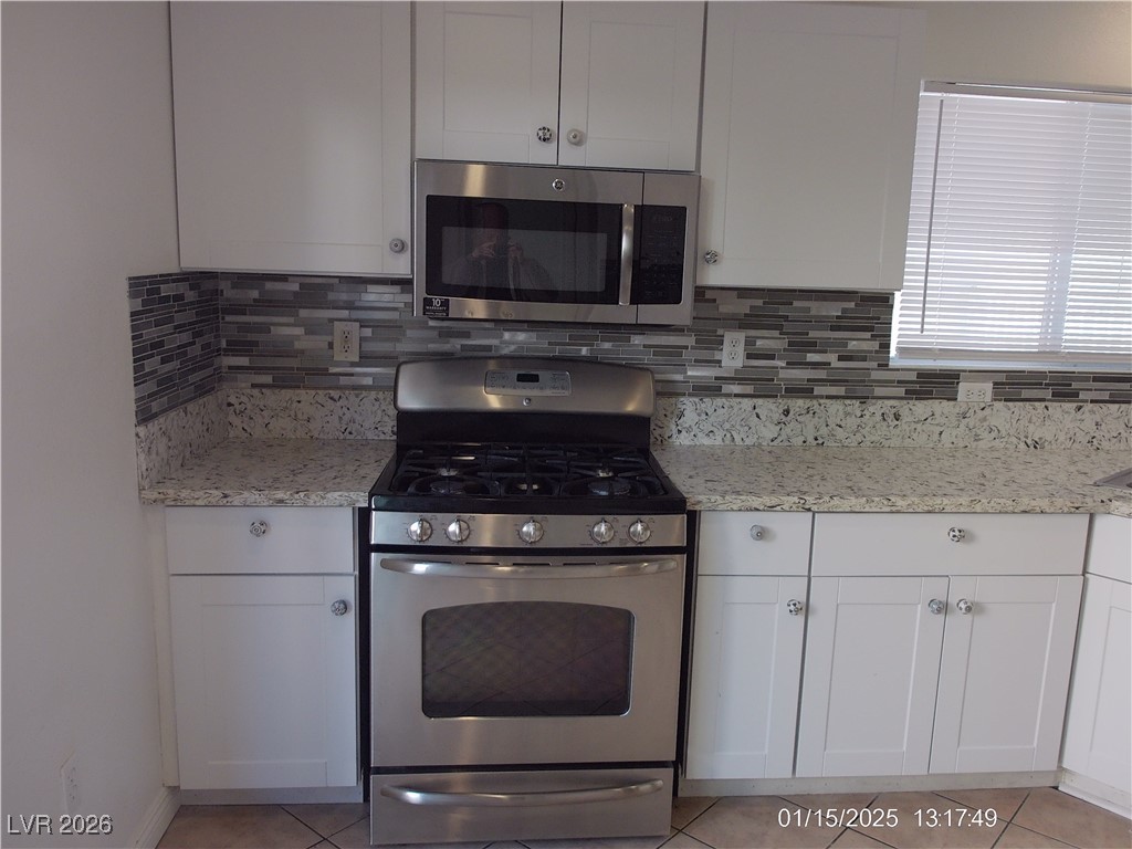 7332 Ribbon Ridge Avenue Las Vegas, NV 89129 - Photo 6 of 28 Kitchen featuring appliances with stainless steel finishes, white cabinets, light stone countertops, and light tile patterned flooring