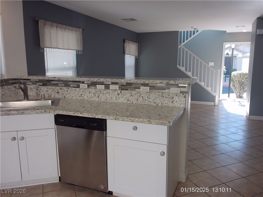 7332 Ribbon Ridge Avenue Las Vegas, NV 89129 - Photo 8 of 28 Kitchen with white cabinets, stainless steel dishwasher, light tile patterned floors, and light stone counters