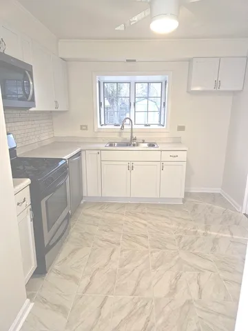 a large white kitchen with granite countertop a sink white cabinets and white appliances