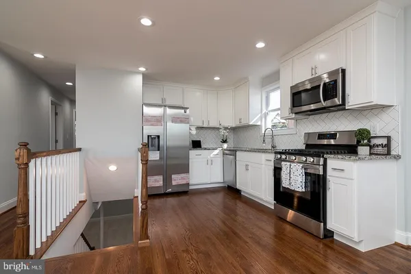 a kitchen with stainless steel appliances granite countertop a refrigerator a stove top oven a sink dishwasher and white cabinets with wooden floor