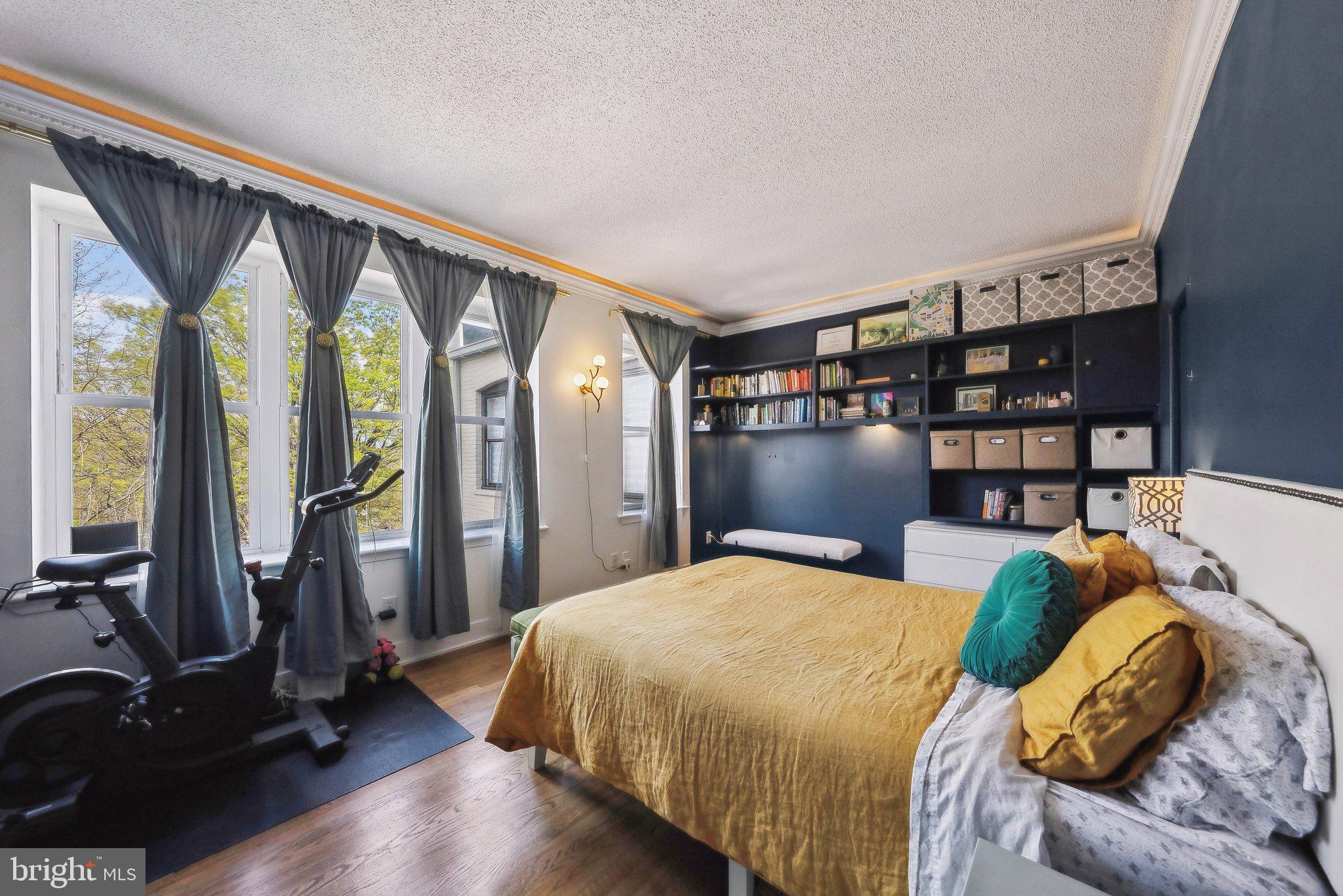2630 Adams Mill Road Northwest, Unit 303 Washington, DC 20009 - Photo 14 of 18 a bedroom with a bed a bookshelf and a large window