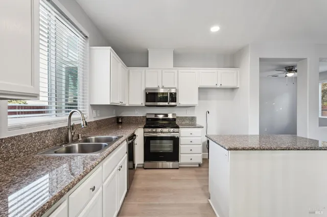a kitchen with granite countertop a sink dishwasher stove and refrigerator with wooden floor