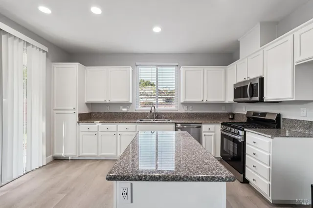 a kitchen with stainless steel appliances granite countertop a stove top oven a sink dishwasher and a refrigerator with wooden floor