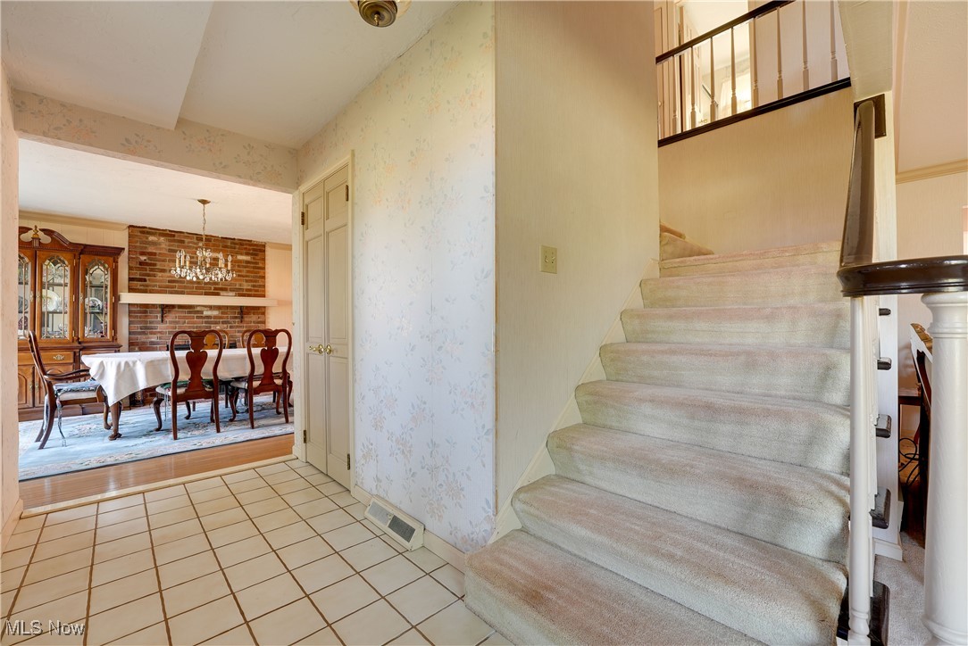 4939 Shankland Road Willoughby, OH 44094 - Photo 11 of 24 Stairs featuring wallpapered walls, tile patterned flooring, and a chandelier