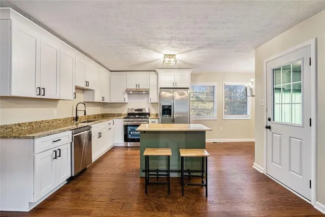 a kitchen with stainless steel appliances granite countertop a stove top oven a sink dishwasher and a refrigerator with wooden floor