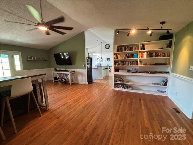 a view of a livingroom with furniture a bookshelf wooden floor and a ceiling fan