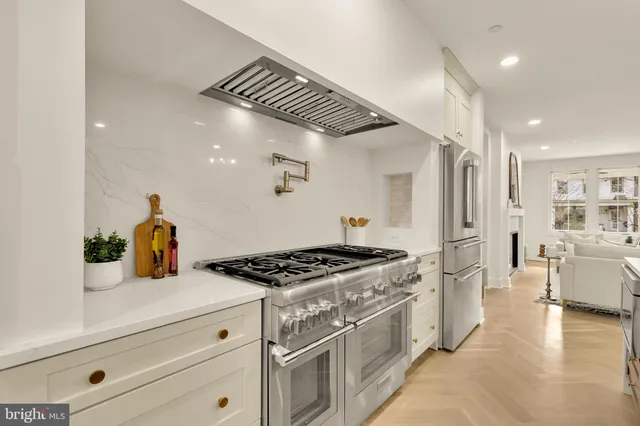 a large white kitchen with a large island oven a stove and a chandelier