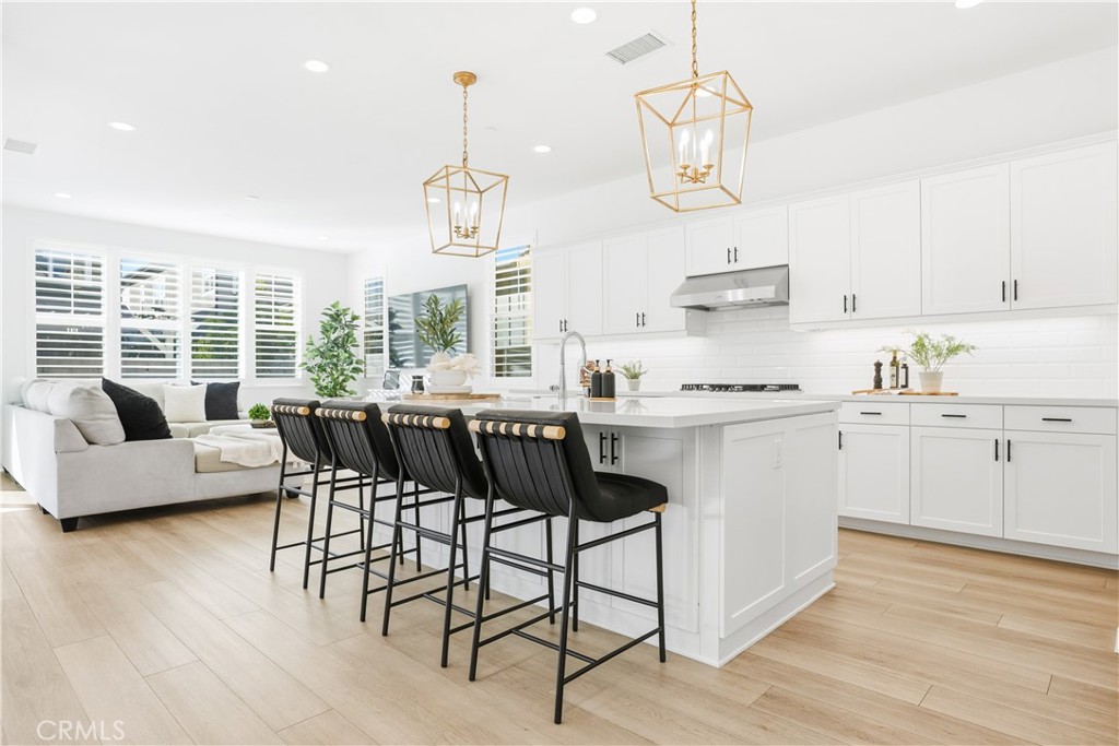 135 Medano Street Rancho Mission Viejo, CA 92694 - Photo 4 of 67 a kitchen with stainless steel appliances kitchen island granite countertop a stove a sink a dining table and chairs with wooden floor