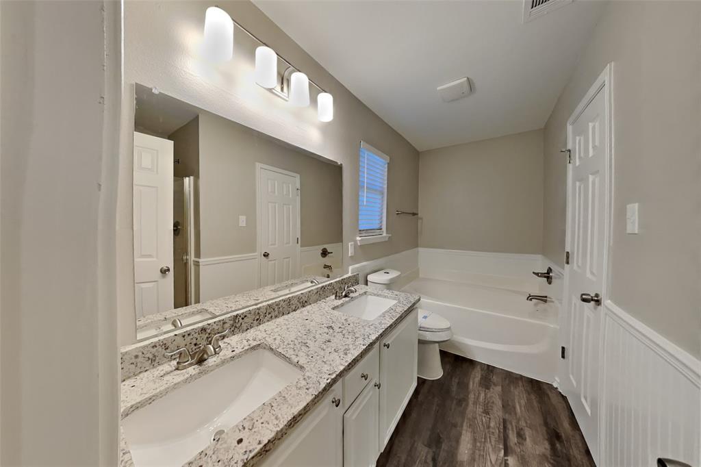 314 South Chestnut Street Forney, TX 75126 - Photo 8 of 18 Bathroom featuring a garden tub, double vanity, dark wood-style floors, and a wainscoted wall