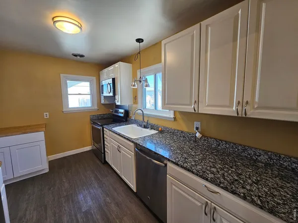 a kitchen with granite countertop a sink a stove cabinets and wooden floor