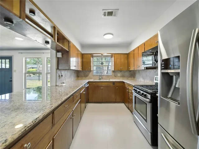 a kitchen with stainless steel appliances granite countertop a refrigerator a sink dishwasher a stove and white countertops with wooden floor