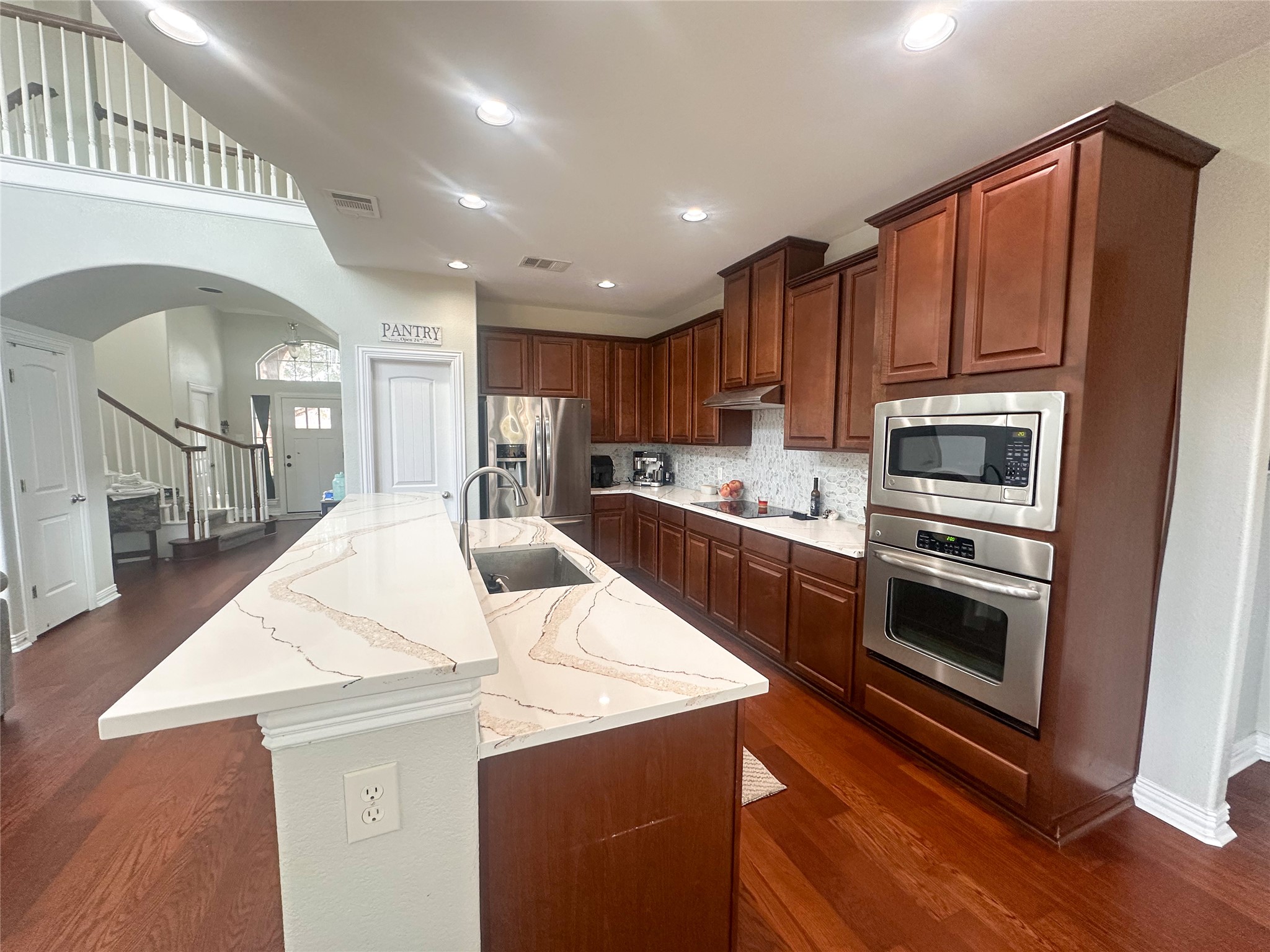 237 Cardinal Drive Paige, TX 78659 - Photo 8 of 37 Kitchen with arched walkways, stainless steel appliances, dark wood finished floors, a large island with sink, and light stone counters