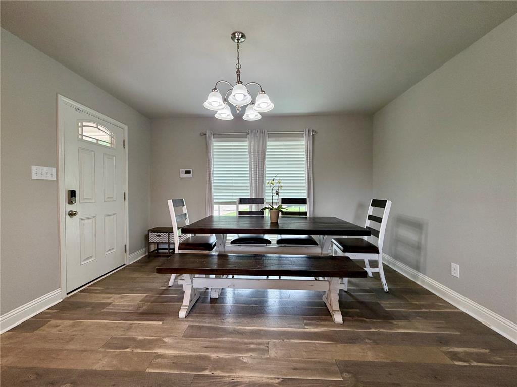 619 Mansfield Road Cleburne, TX 76031 - Photo 13 of 19 Dining area featuring wood-finish flooring, a contemporary chandelier, and a white paneled entry door with an arched transom