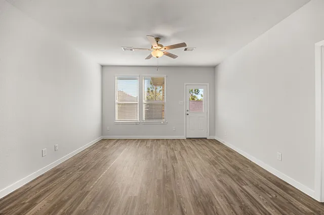 an empty room with wooden floor chandelier fan and windows