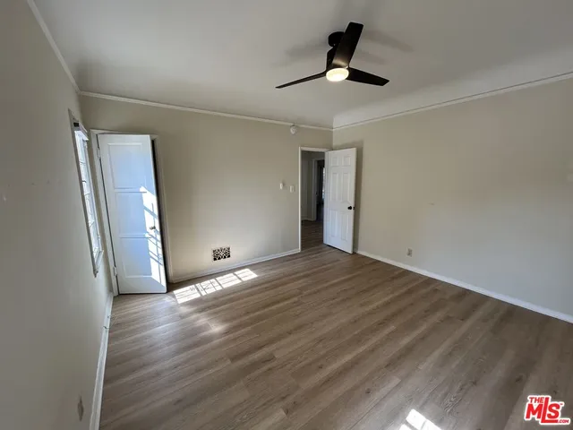 a view of an empty room with wooden floor and a ceiling fan