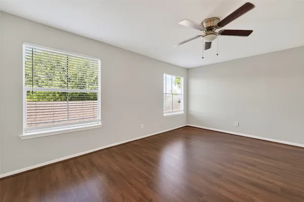 an empty room with wooden floor a ceiling fan and windows
