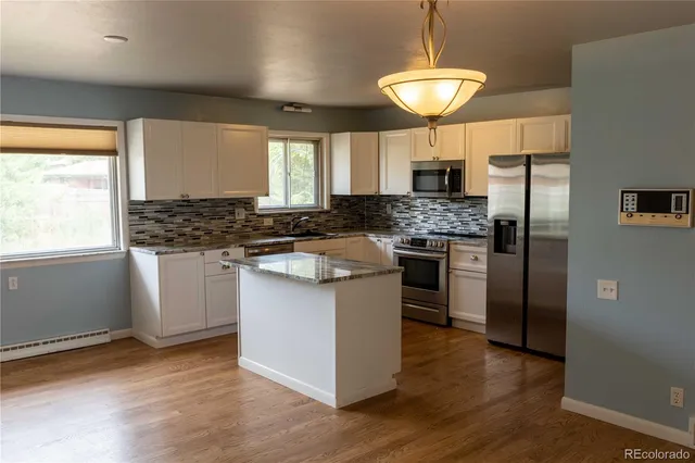 a kitchen with kitchen island granite countertop a stove a sink a refrigerator and white cabinets with wooden floor