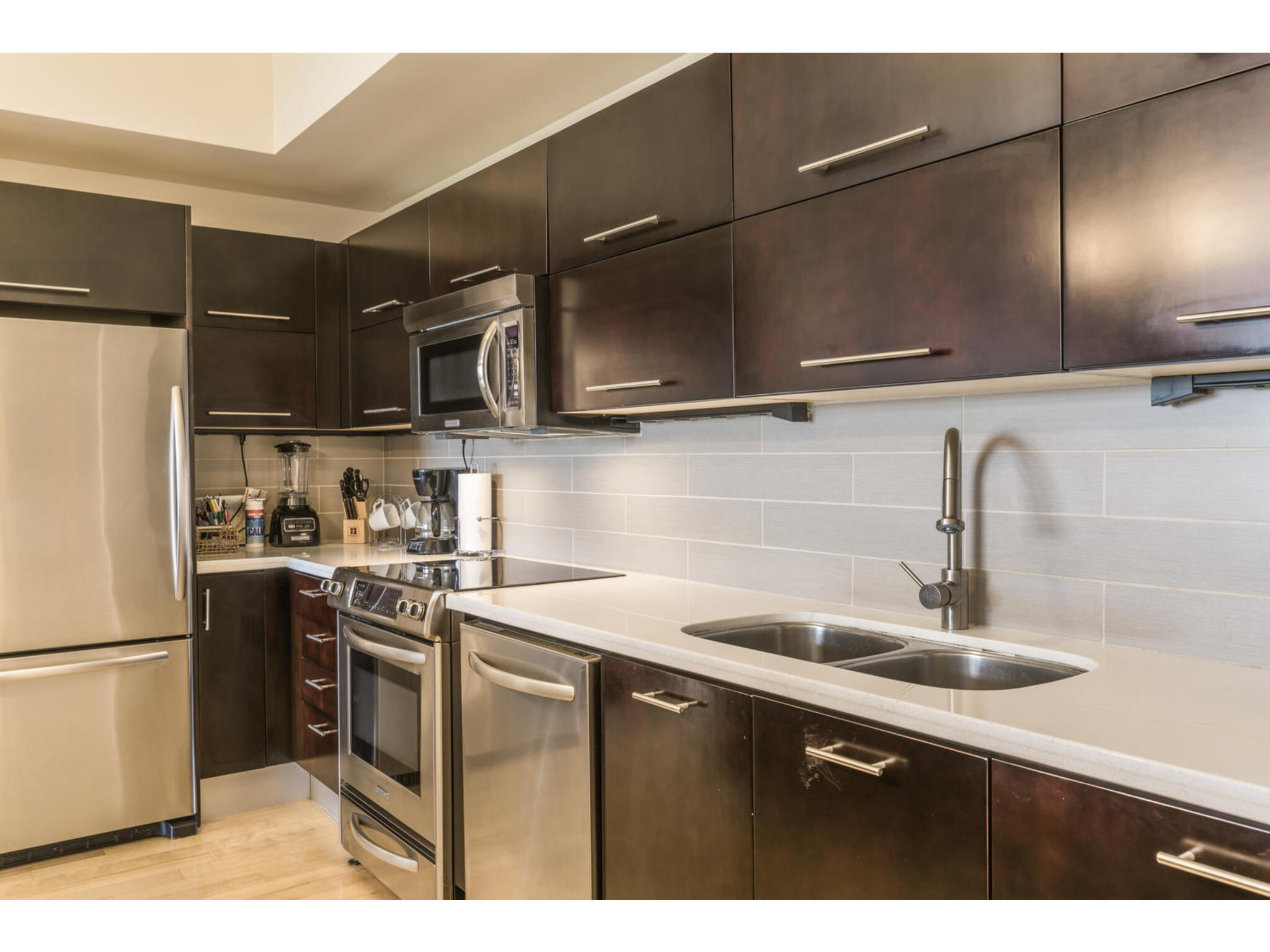 603 Davis Street, Unit 902 Austin, TX 78701 - Photo 11 of 21 Kitchen with stainless steel appliances, dark wood finish cabinetry, decorative backsplash, light wood-style flooring, and light stone countertops