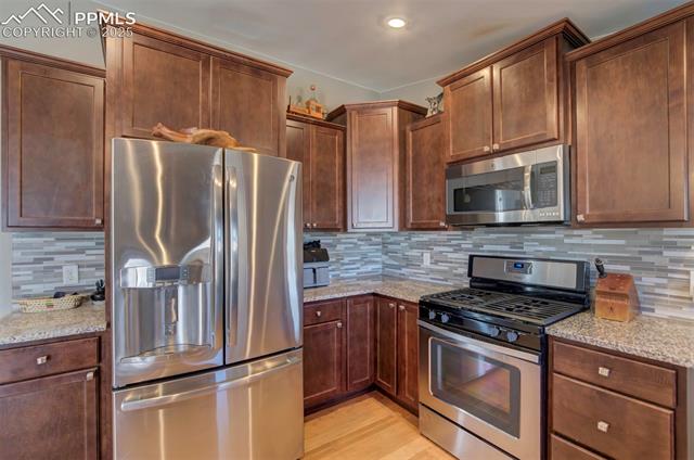 5860 Curtis Road Peyton, CO 80831 - Photo 13 of 28 Kitchen featuring stainless steel appliances, light stone countertops, decorative backsplash, and light wood finished floors