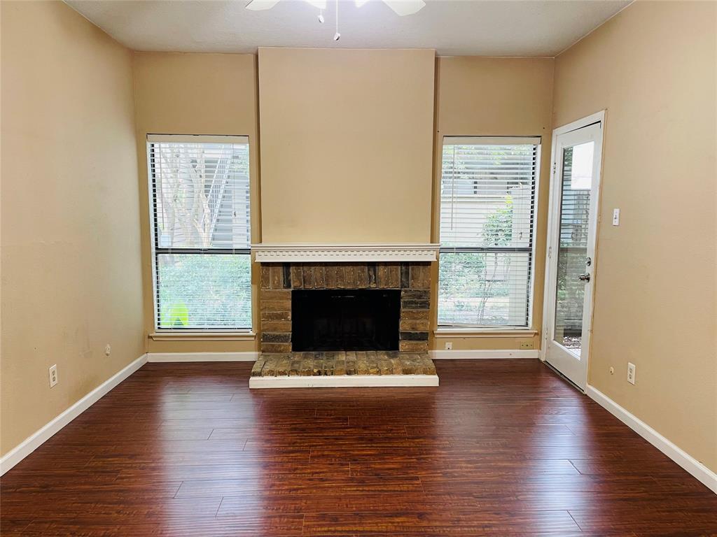 an empty room with wooden floor fire place and windows