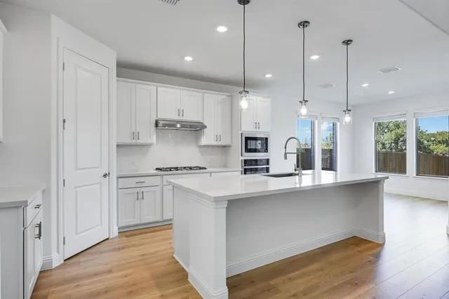 a kitchen with stainless steel appliances granite countertop a sink a stove a refrigerator and white cabinets