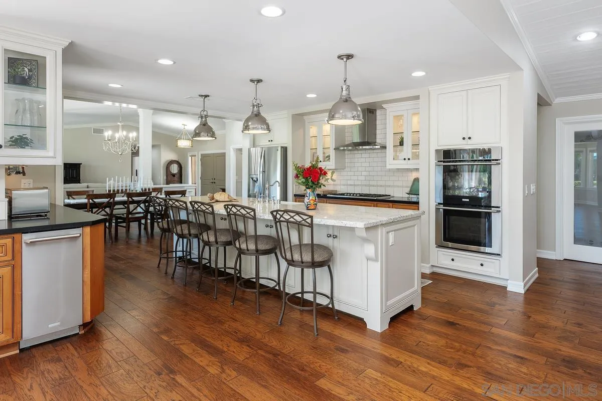 13627 Poway Springs Road Poway, CA 92064 - Photo 11 of 60 a large white kitchen with lots of counter space wooden floor stainless steel appliances and living room view