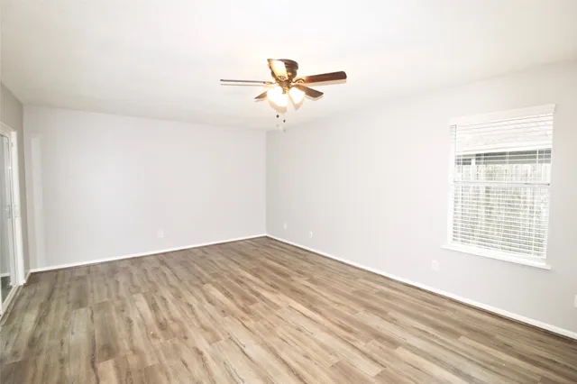 an empty room with wooden floor fan and windows
